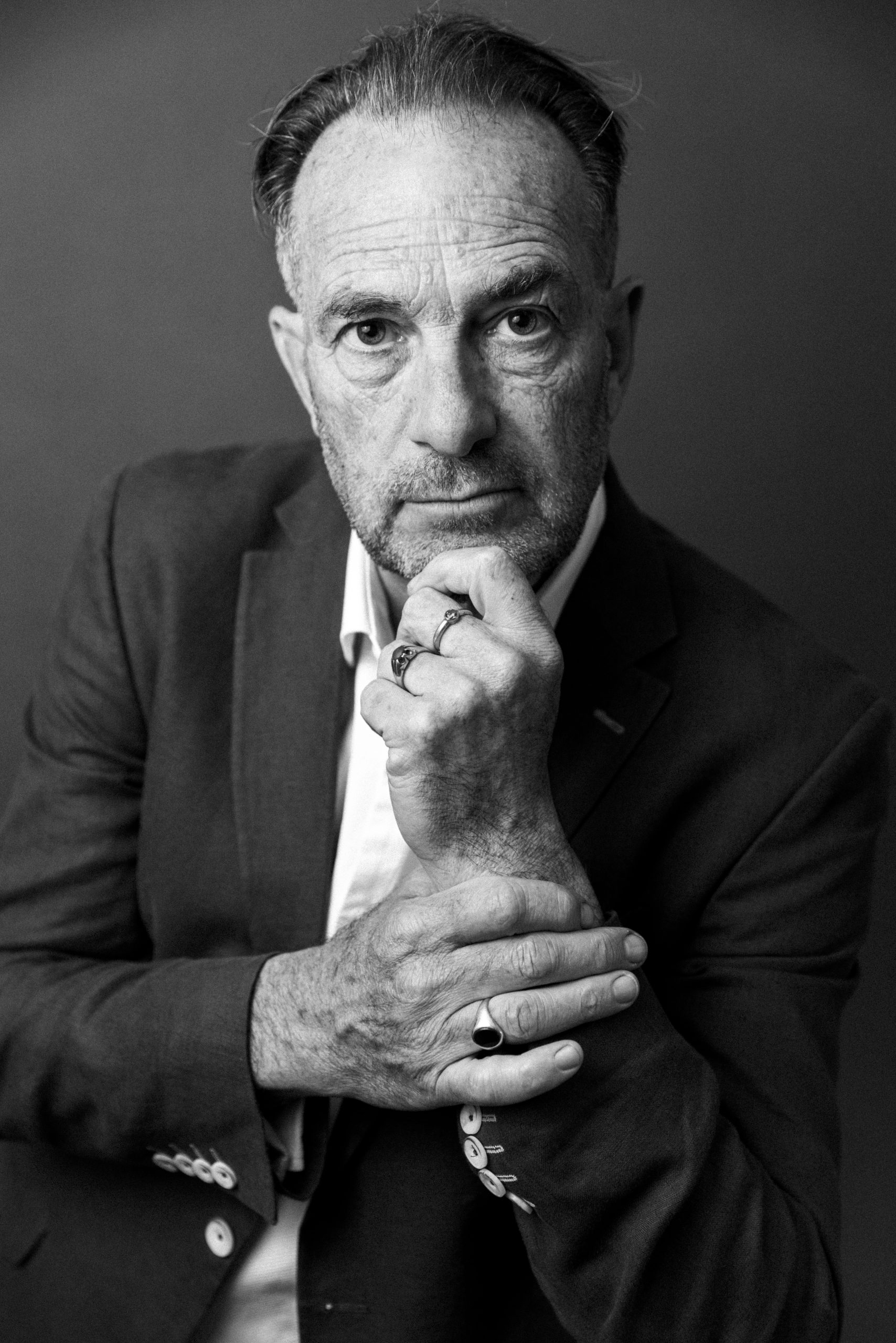 Black and white portrait of a man in glasses and a suit jacket, resting his chin on his hand while looking thoughtfully toward the camera. The close-up composition and dramatic lighting create a reflective, professional atmosphere.