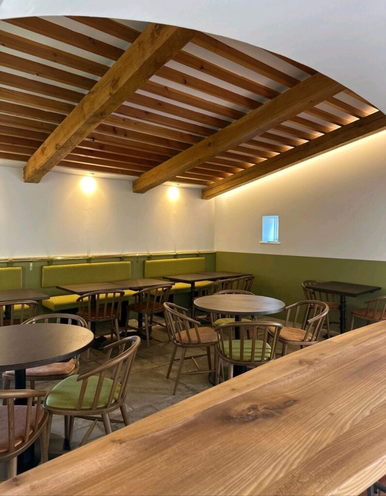 Hospitality interior designed by Cooper8, with timber furniture, green banquette seating and exposed roof beams.