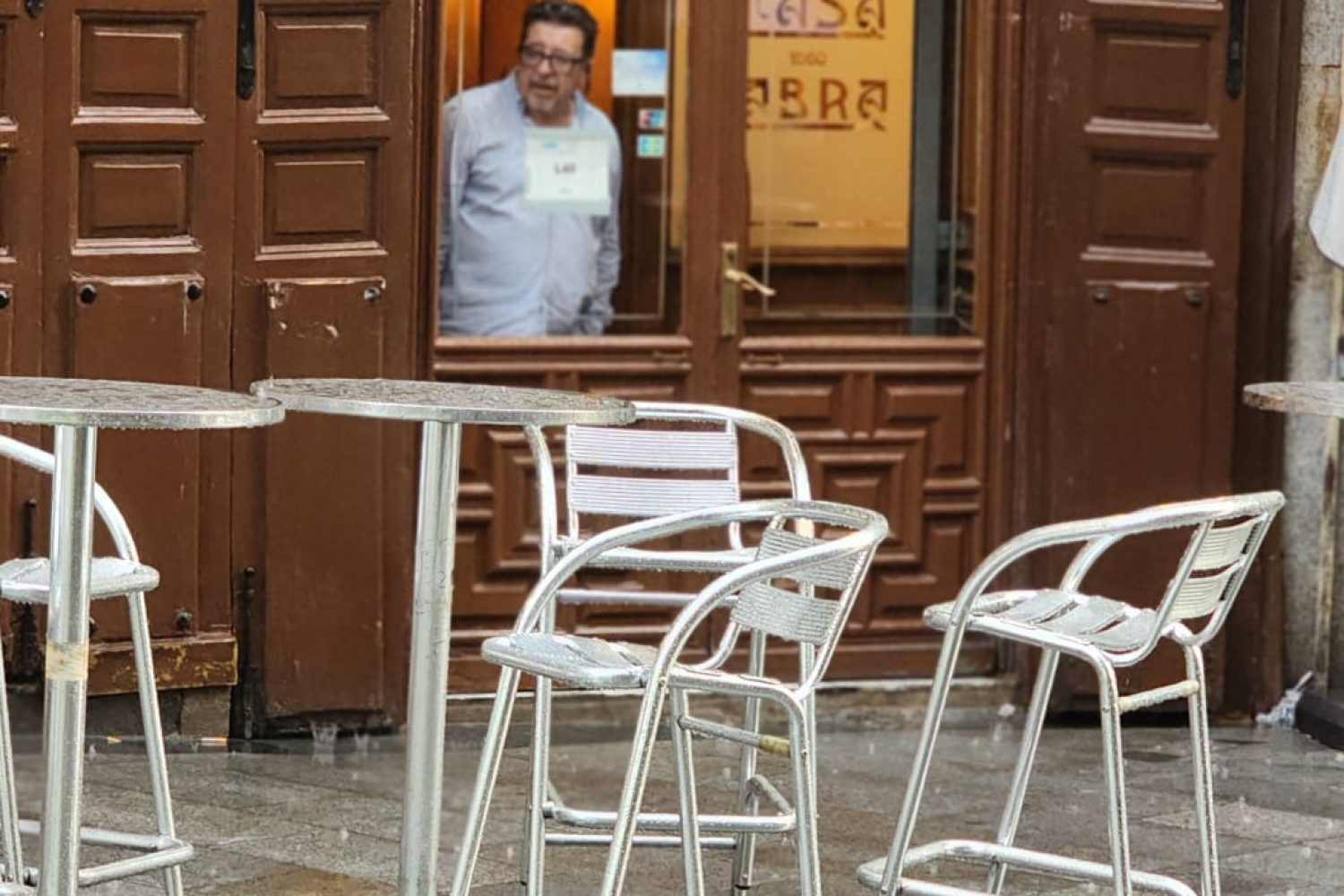 Exterior of Casa Labra in Madrid during a summer rainstorm, with a chef in white uniform looking out from the window.