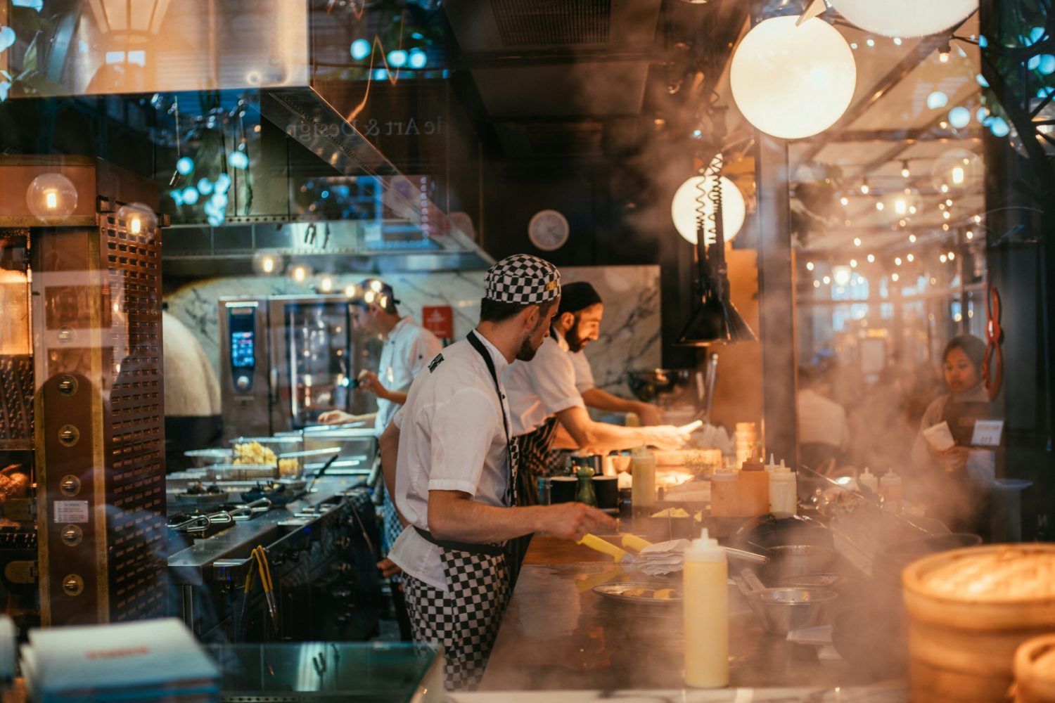 Busy restaurant kitchen during service with chefs preparing food at a counter, showing a high-pressure working environment